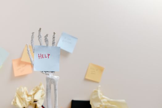 Skeleton hand holding a sticky note with 'HELP' written, against colorful notes background.