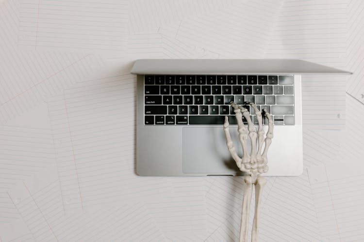 Overhead Shot Of A Skeleton Hand Typing On A Laptop