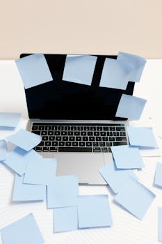 A laptop covered with blue sticky notes, symbolizing a busy and disorganized workspace.