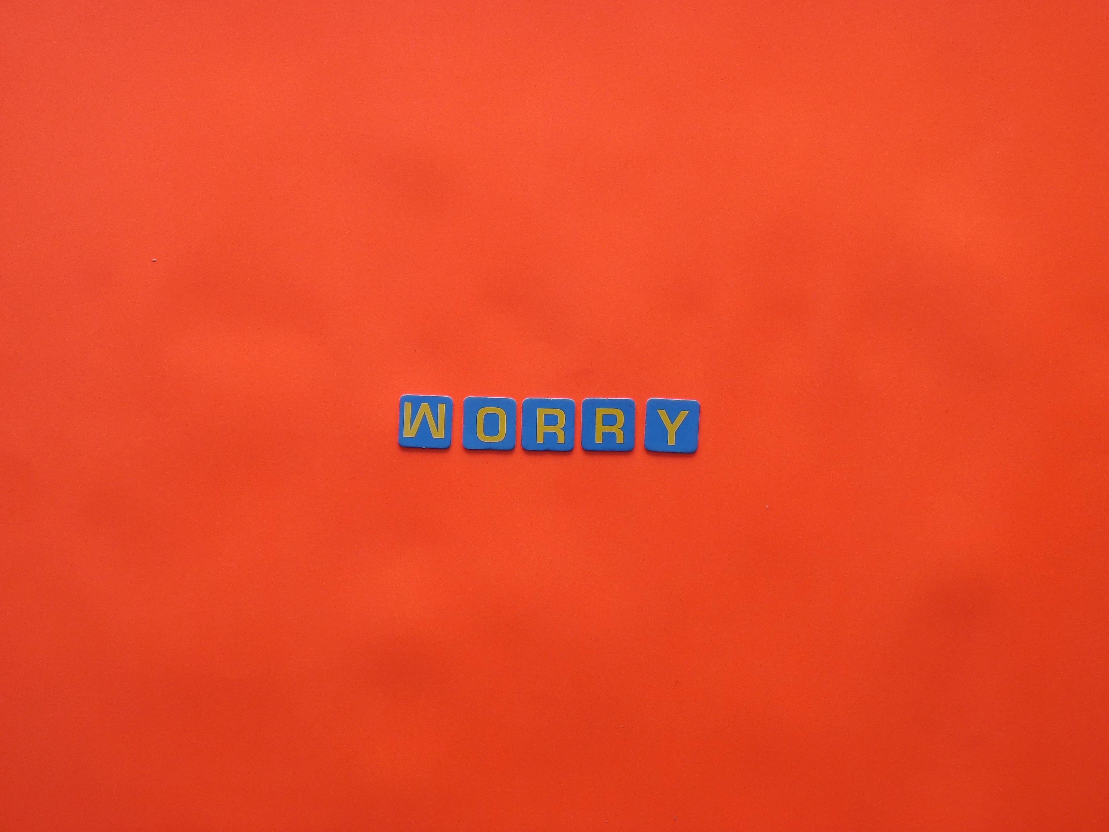 Blue letter blocks spelling 'worry' on a bold orange background. Bright and conceptual design.