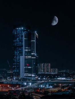 Stunning view of Kuala Lumpur's cityscape under a night sky with a luminous half moon above.