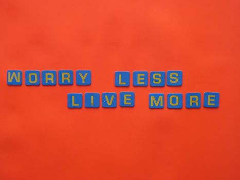Blue tiles spelling 'Worry Less Live More' on an orange background for a motivational theme.