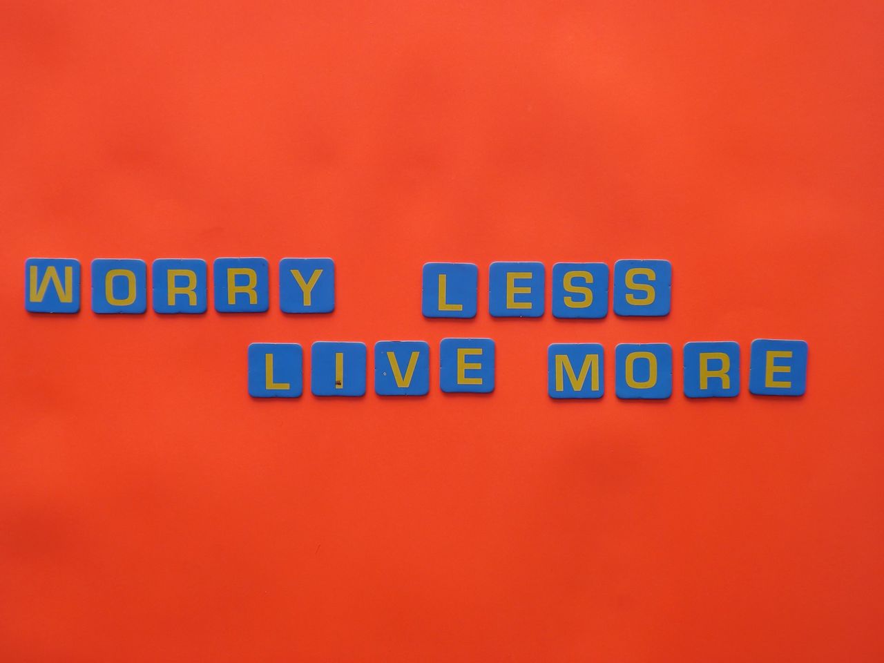 blue tiles spelling worry less live more on an orange background for a