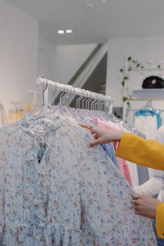 Woman browsing floral print dresses on a clothing rack indoors in a fashion store.