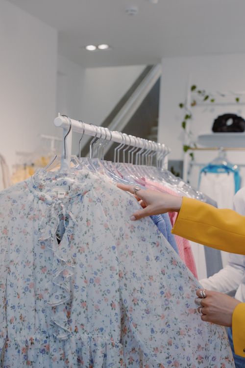 Free Woman browsing floral print dresses on a clothing rack indoors in a fashion store. Stock Photo