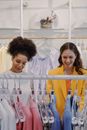 Women Smiling While Choosing Clothes on Hangers