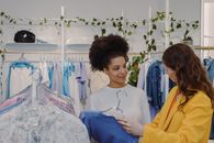Woman in White Shirt Smiling While Choosing Clothes with a Friend