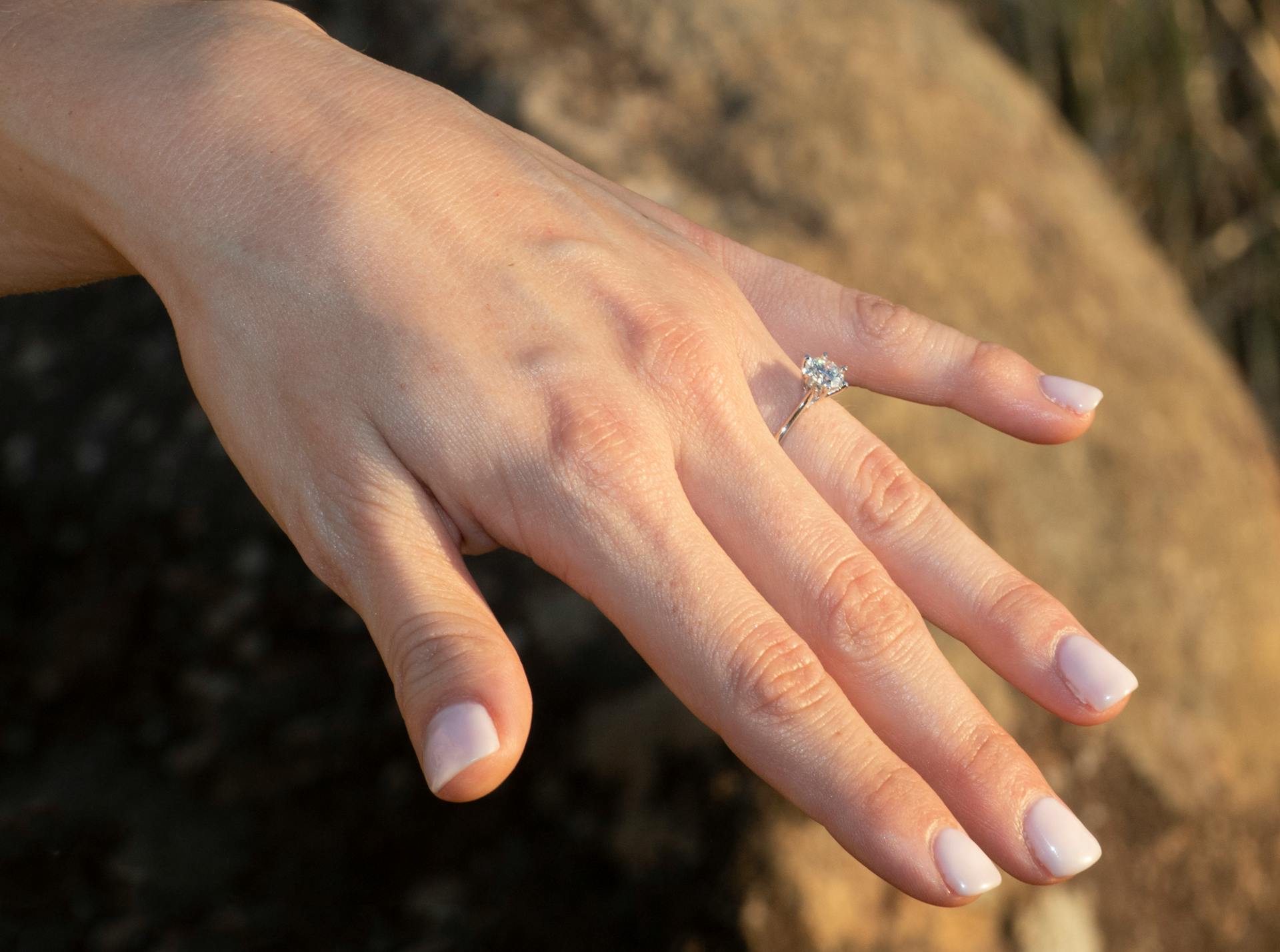 Close-up of a hand showcasing a beautiful diamond engagement ring in natural light.