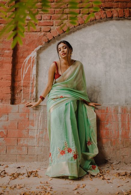 Beautiful Indian woman in traditional green saree posing by a rustic brick wall.