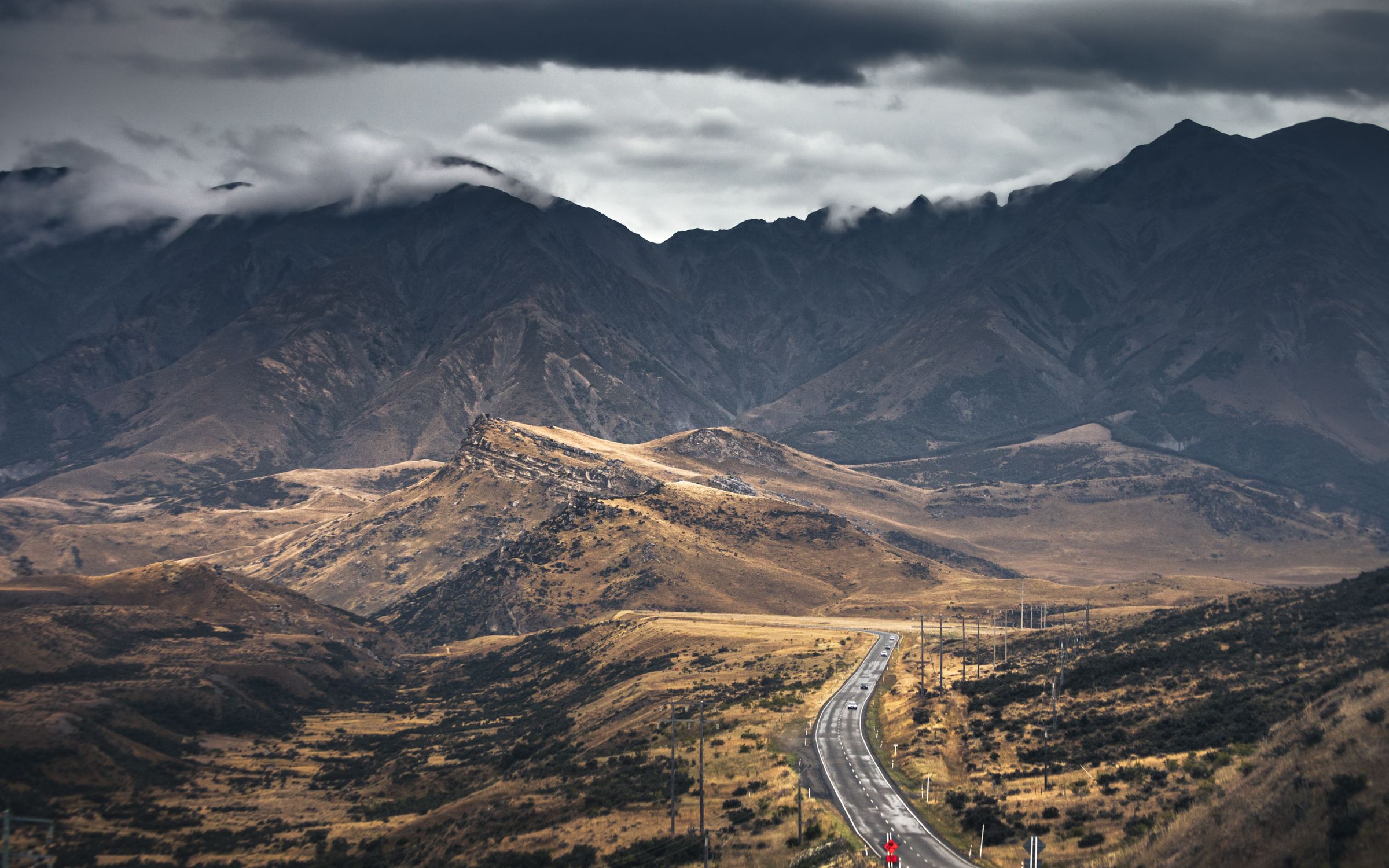 Beautiful scenic road winding through mountains in New Zealand under dramatic clouds.