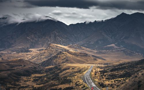Free Beautiful scenic road winding through mountains in New Zealand under dramatic clouds. Stock Photo