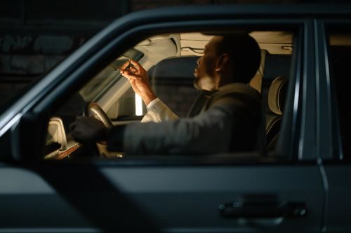Free A man sitting inside a car at night adjusting the rearview mirror. Interior illuminated with selective focus. Stock Photo