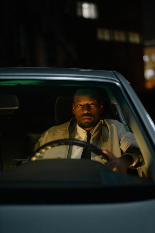 Free An adult man sits inside a car at night, focused on driving through the cityscape. Stock Photo
