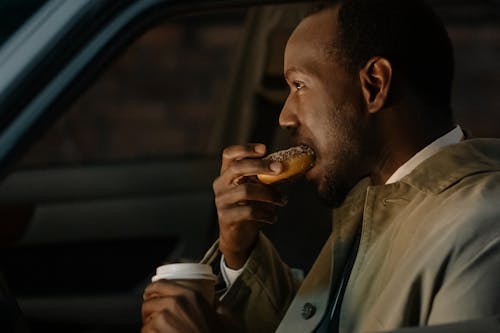 Man Sitting Inside a Vehicle Eating Donut with Cup of Coffee