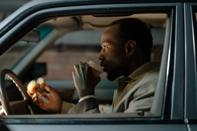 Man Sitting Inside A Car Holding Donut And Drinking Coffee