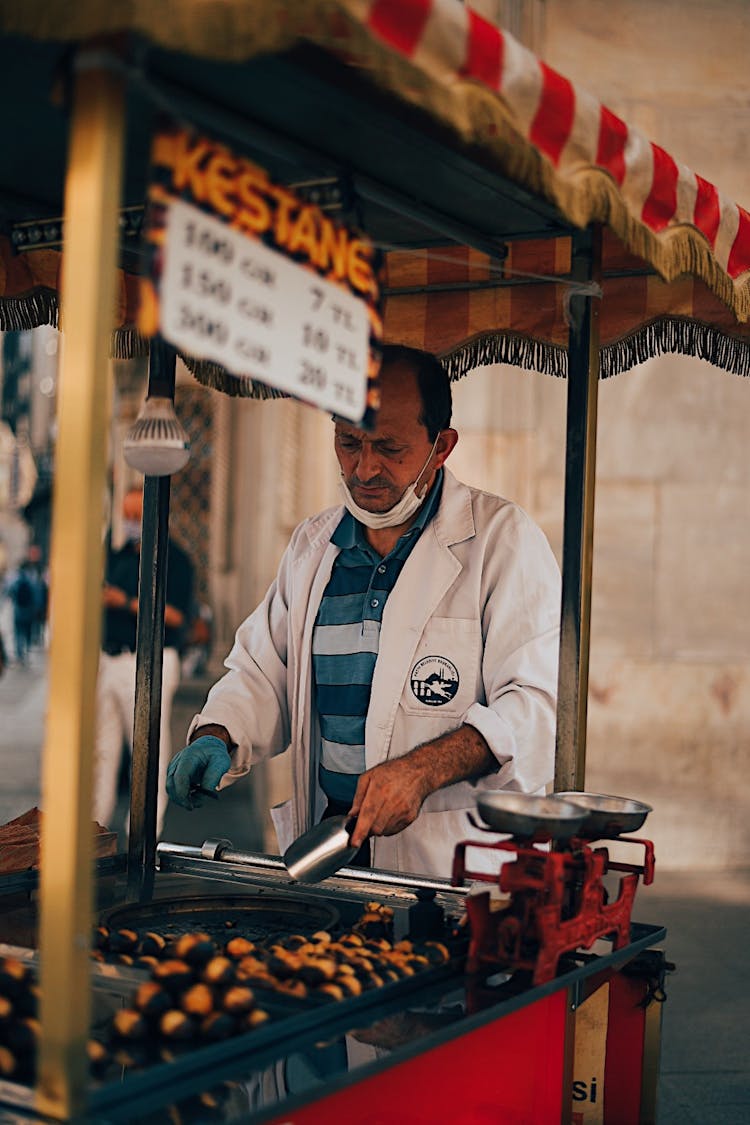 A Man In White Long Sleeve Jacket Cooking Street Food On A Cart