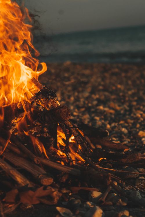 Free Warm bonfire flames lighting up a pebbly beach, creating a cozy outdoor evening ambiance. Stock Photo