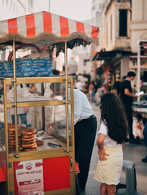 Free Woman in White Long Sleeve Shirt Standing in Front of Food Stall Stock Photo