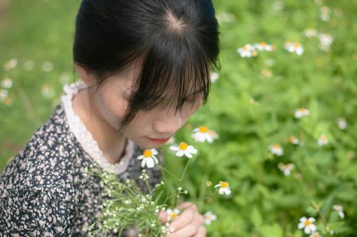 Free A woman in a floral dress holding daisies in a lush green field. Stock Photo