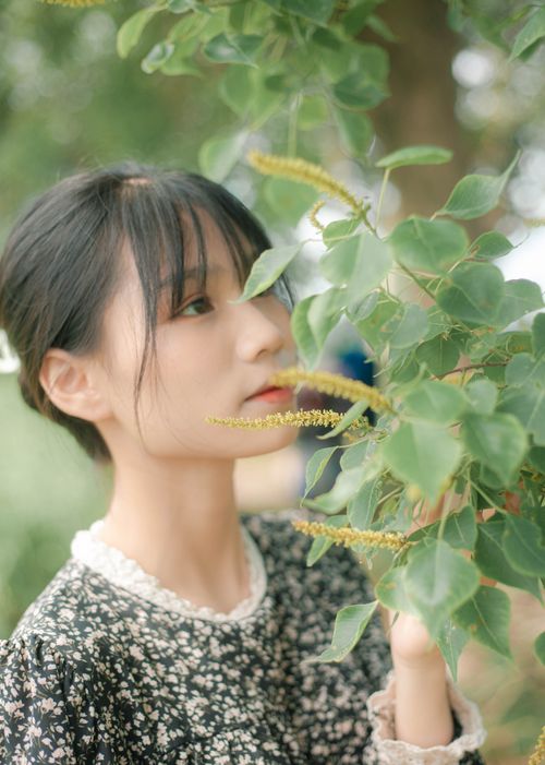 Free Young woman in a floral dress gently touching green leaves outdoors. Stock Photo