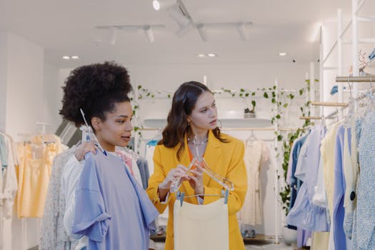 Two women shopping for trendy clothes in a stylish boutique with plant decor.