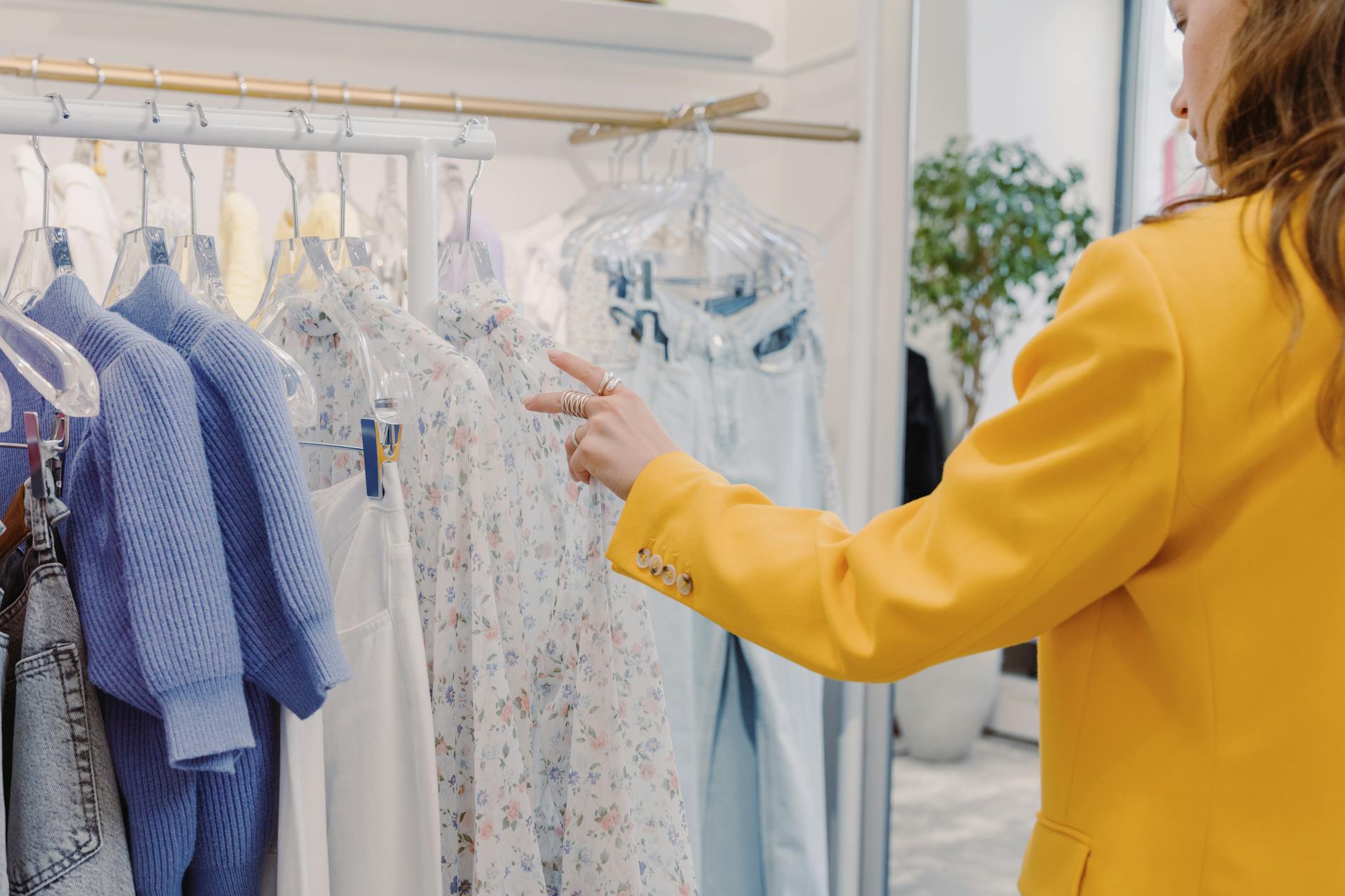 A customer in a yellow blazer browses stylish clothing in a chic boutique setting.