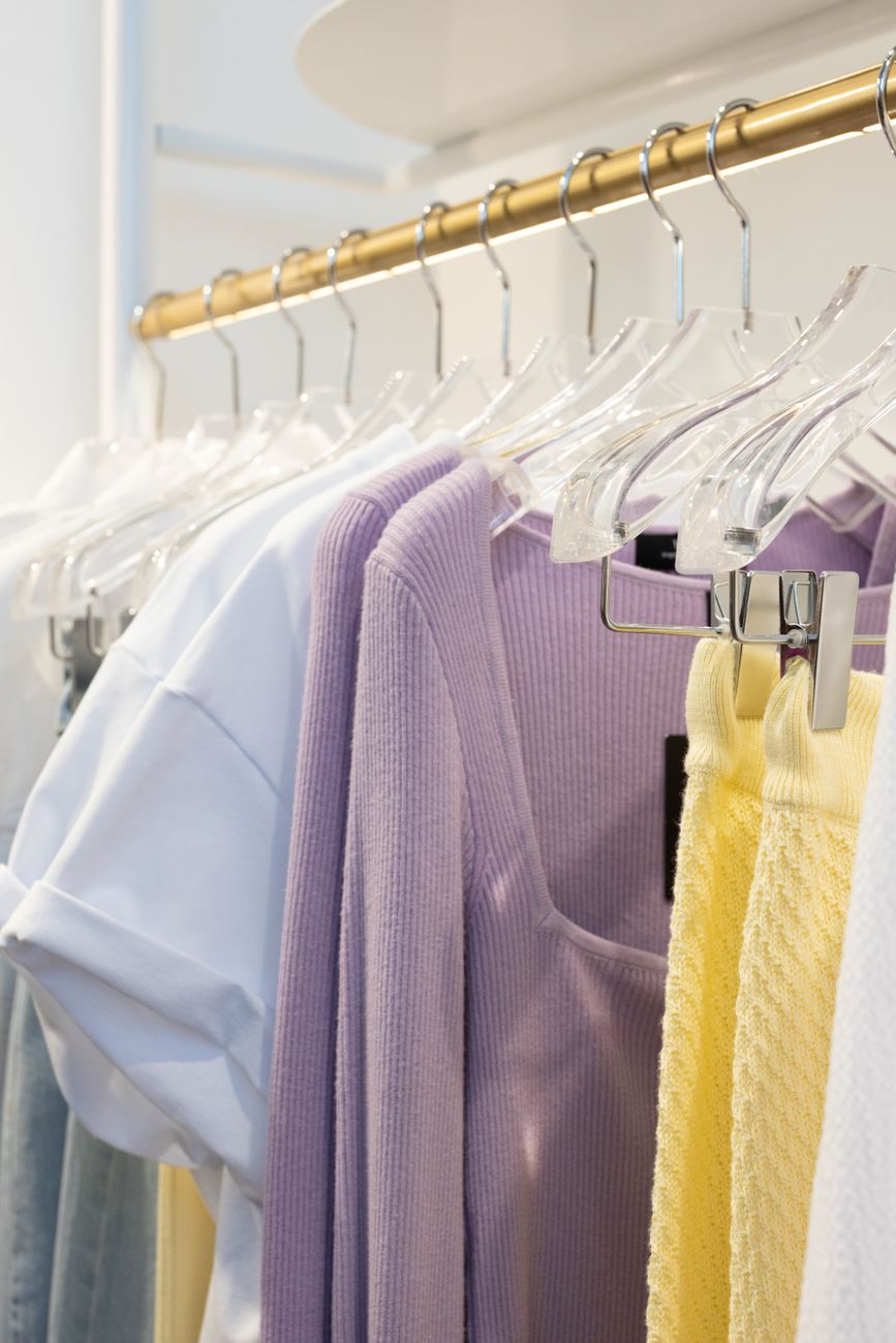 A collection of pastel-colored clothes hanging on a gold wardrobe rack in an indoor boutique.