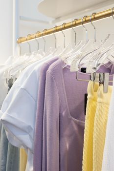 A collection of pastel-colored clothes hanging on a gold wardrobe rack in an indoor boutique.