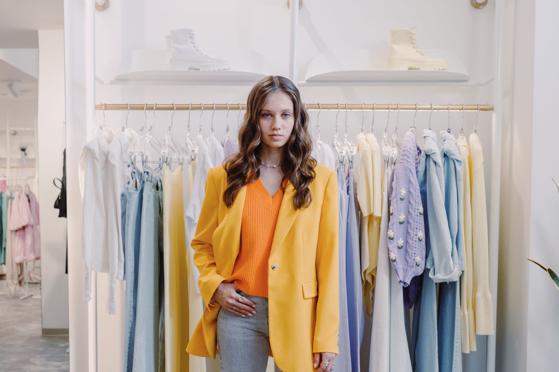 Stylish woman wearing orange and yellow in a chic boutique, surrounded by hanging clothes.