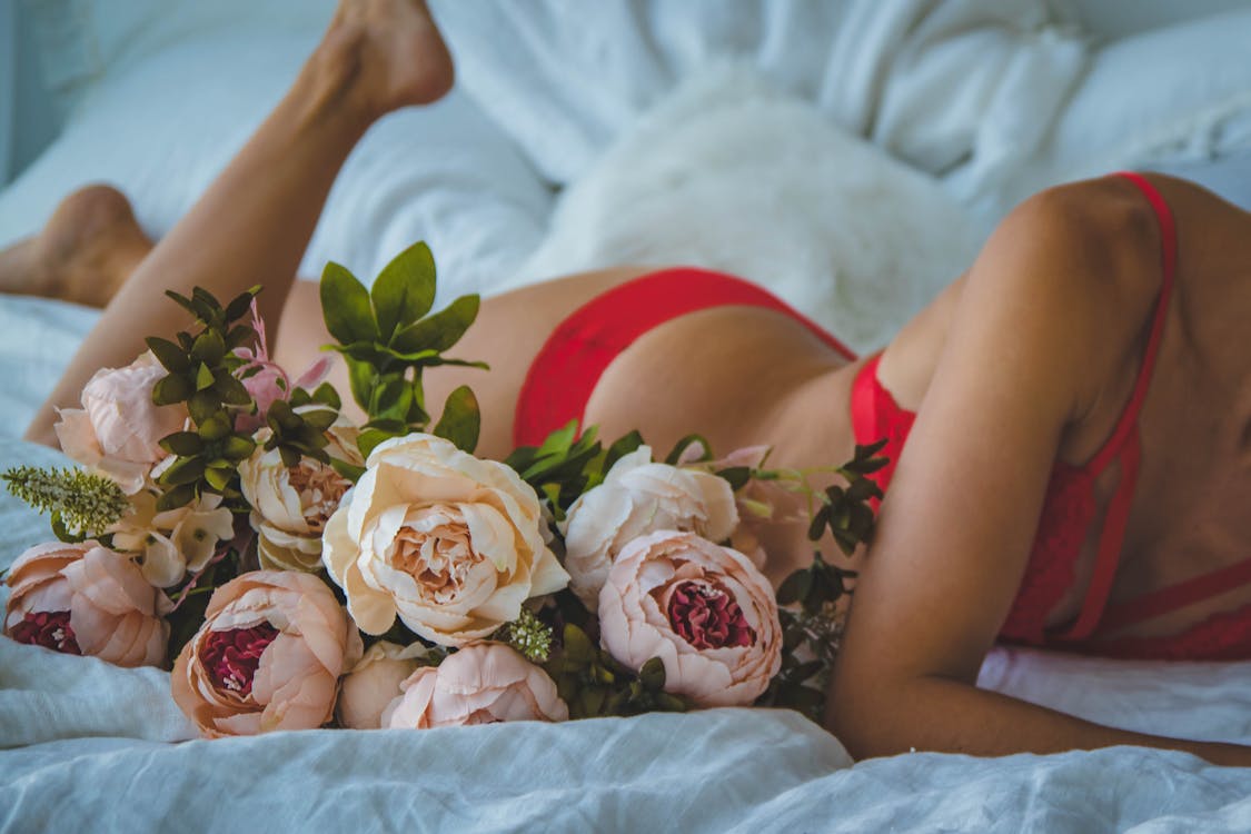 Free Woman in Red Two-piece Bikini Lying on Bed Beside of White and Pink Roses Stock Photo