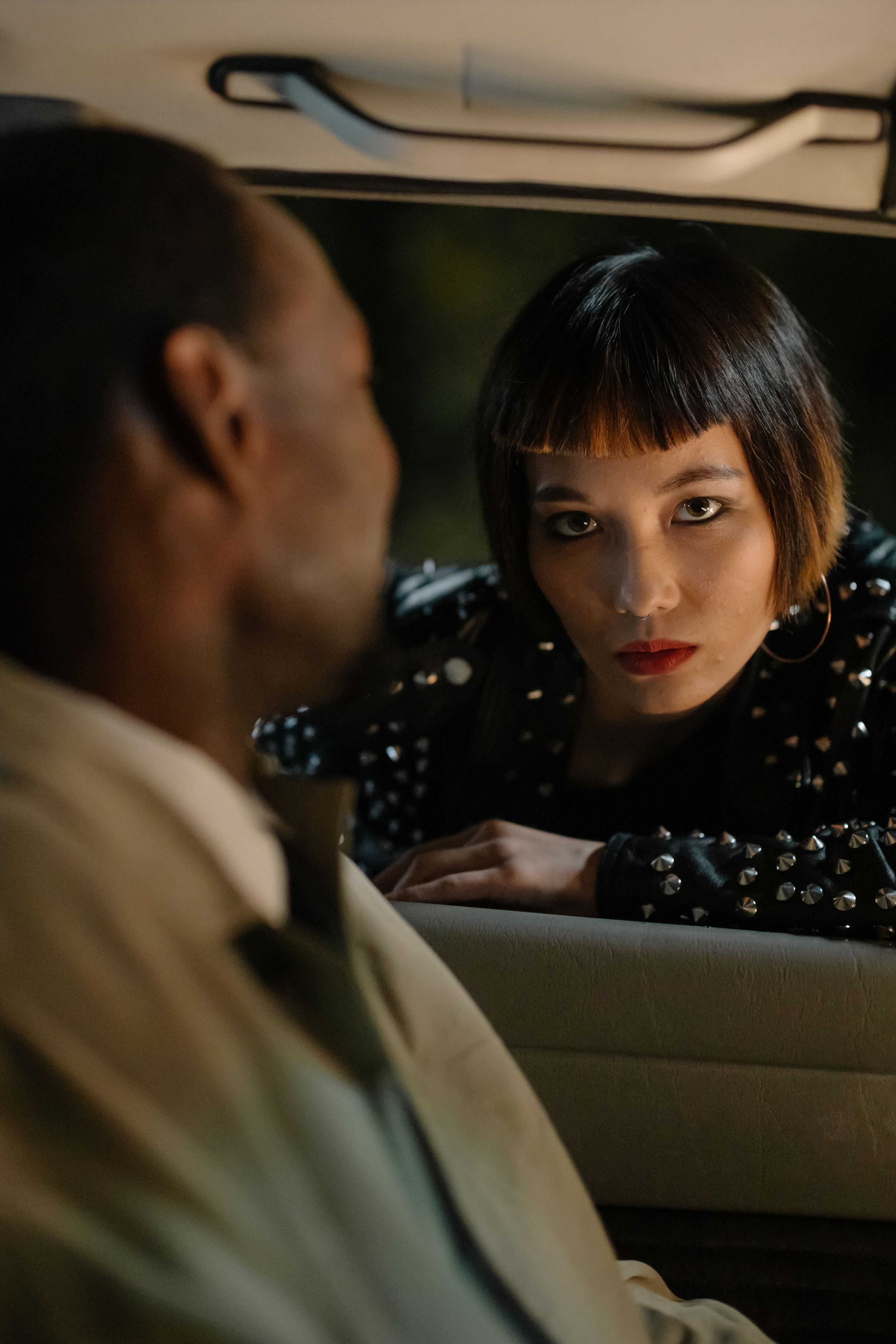 A stylish woman leaning into a car window, engaging with the driver at night.