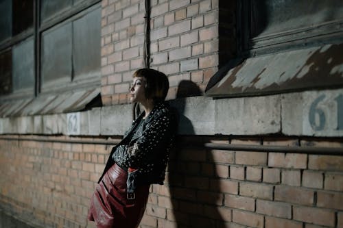 Free Woman in Black Leather Jacket Standing Against a Brick Wall Stock Photo