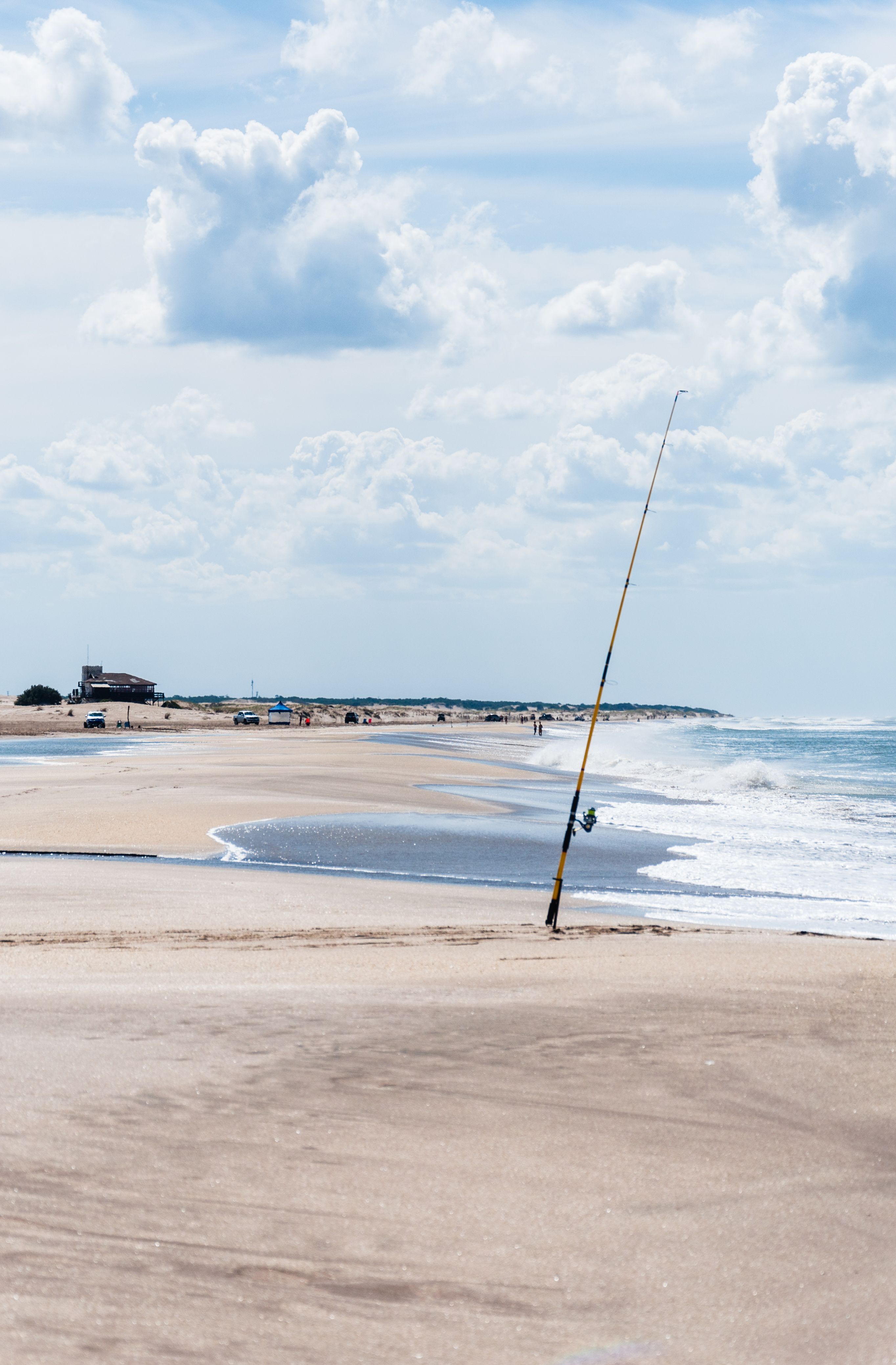 Tranquil beach scene with fishing rod, sandy shore, and gentle waves under a blue sky.