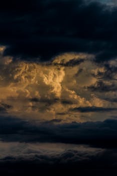 Dark and dramatic storm clouds lit by the golden hues of sunset, creating a moody sky.