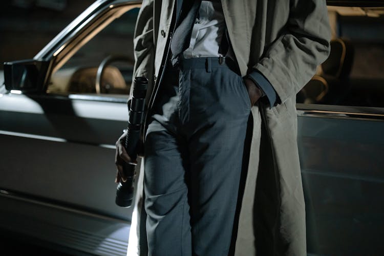 Close-Up Shot Of A Person In Beige Coat Holding A Flashlight While Leaning On The Car