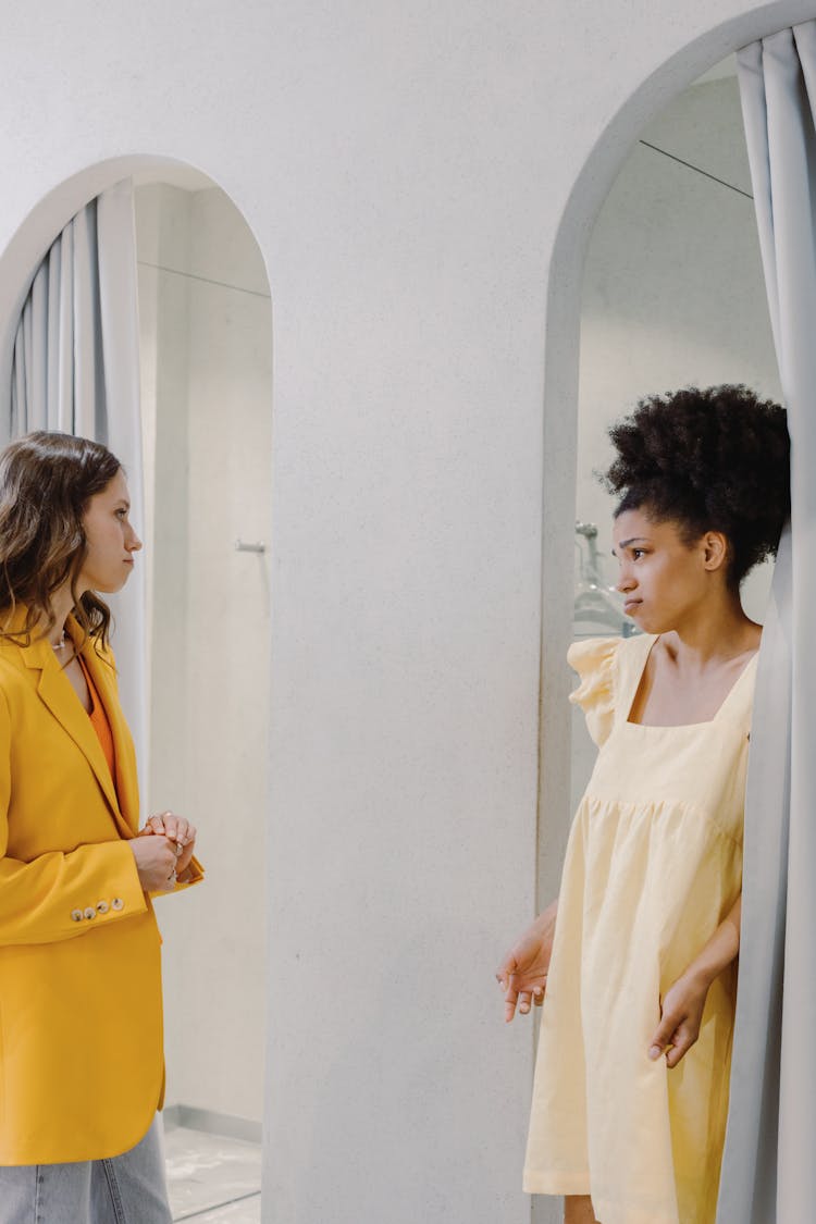 Woman In Yellow Blazer Looking At A Woman Wearing A Dress