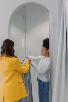 Two women in a clothing store fitting room trying on clothes with hangers.