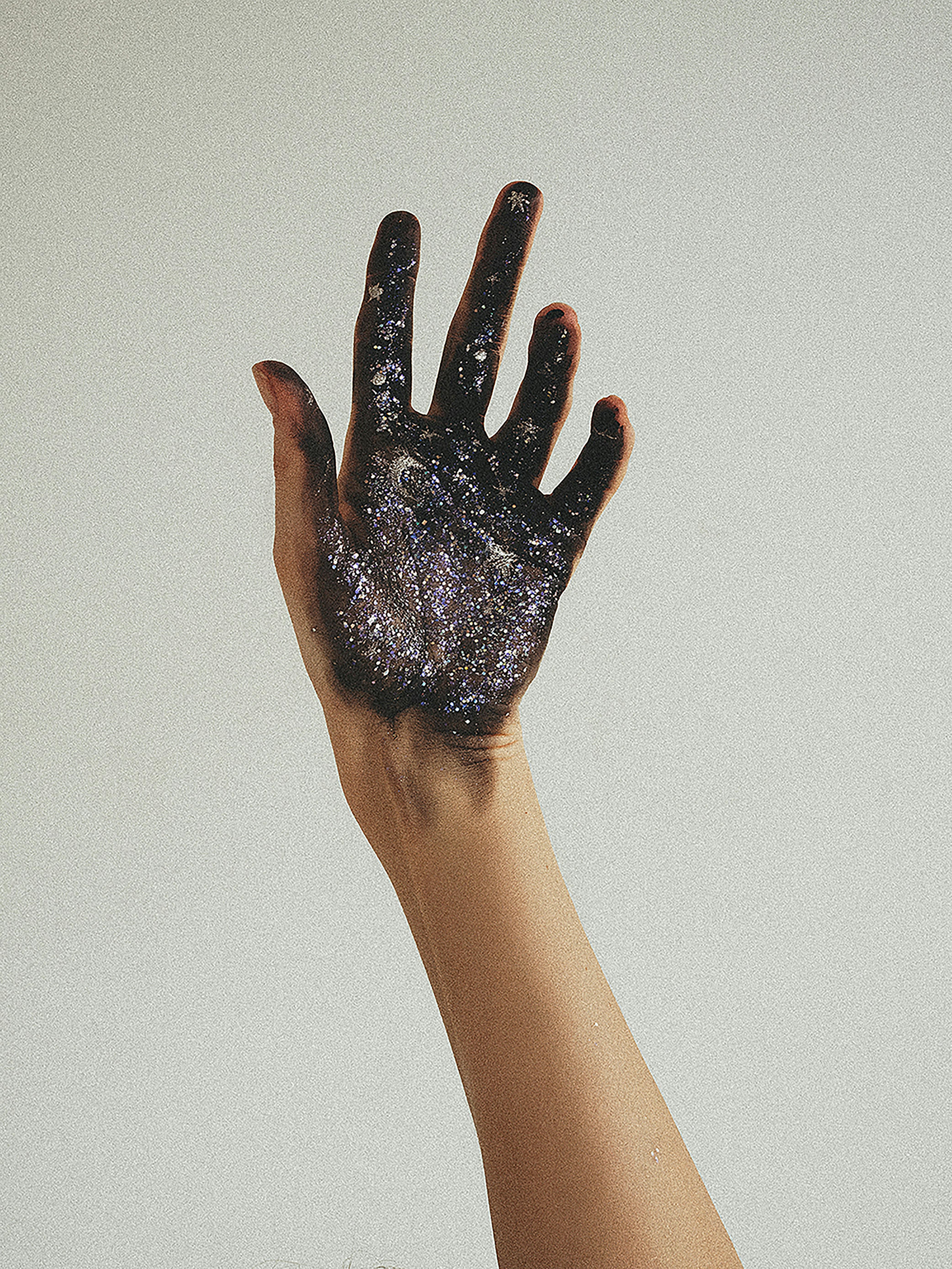 shot of a hand painted with dark glitter against white wall