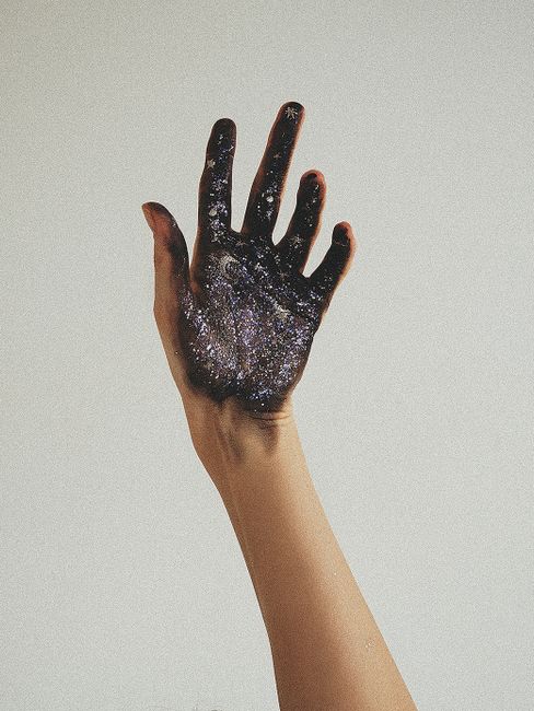 A creative photo of a glitter-painted hand against a white wall, showcasing artistic expression.