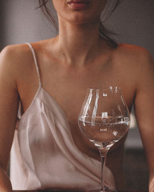An elegant portrait of a woman in a satin top with a glass of mineral water indoors.