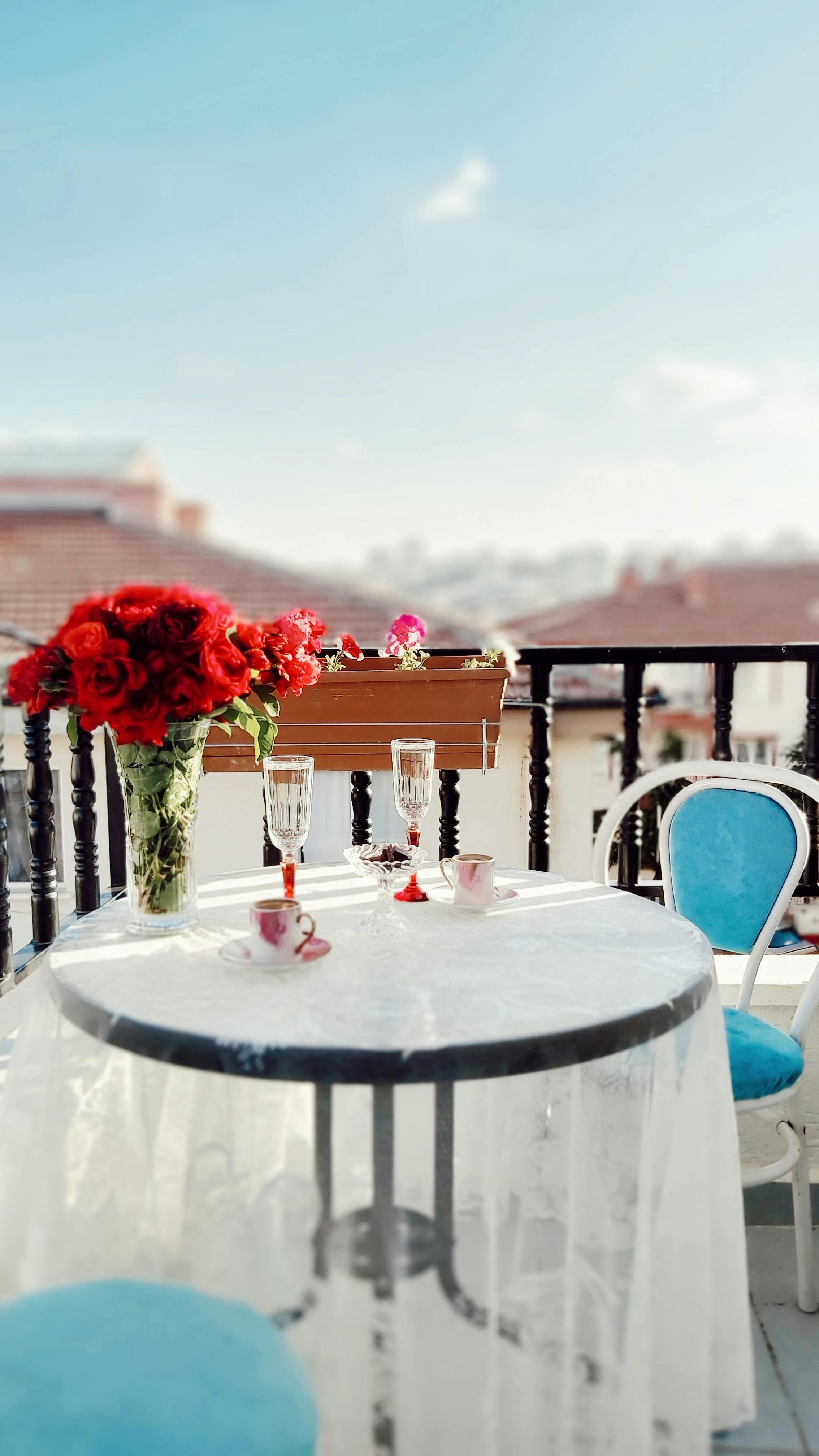 A beautifully set balcony table with red roses and a scenic view, perfect for a romantic meal.