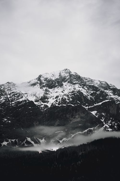 Free Majestic view of a snow-covered mountain peak beneath a cloudy sky, creating a dramatic and serene atmosphere. Stock Photo