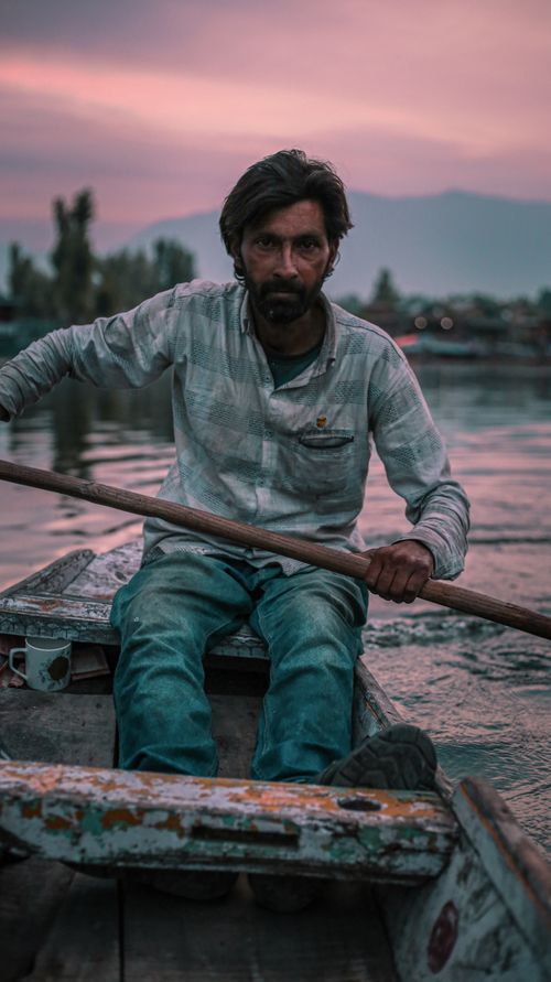 Free A bearded man rowing a boat at sunset on a tranquil lake with serene surroundings. Stock Photo