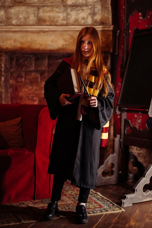 Young Woman Standing in Black Cape Holding a Book and Wand