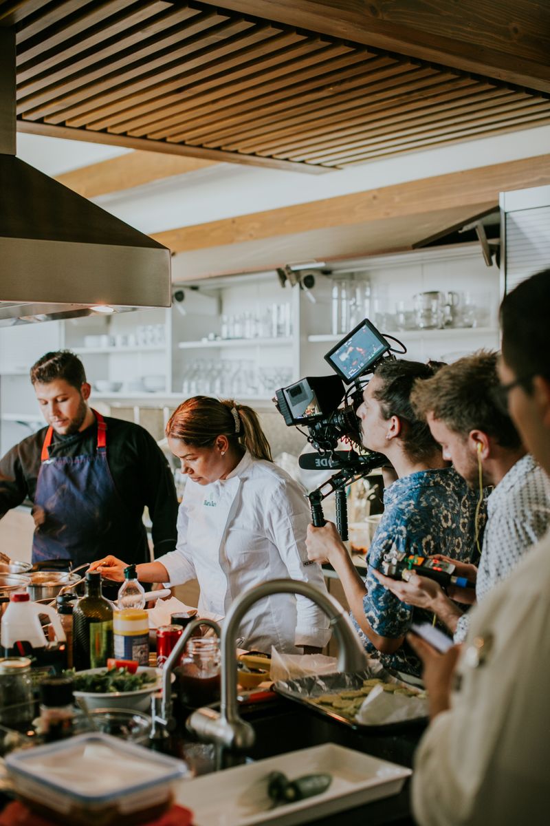 Chefs are filmed cooking in a modern kitchen, showcasing culinary skills for a show.