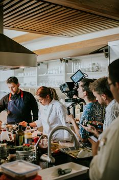 Chefs are filmed cooking in a modern kitchen, showcasing culinary skills for a show.