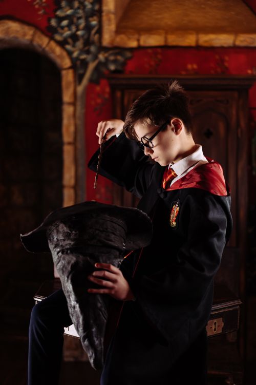 Free Boy dressed as a wizard with wand and sorting hat, in a dimly lit room. Stock Photo