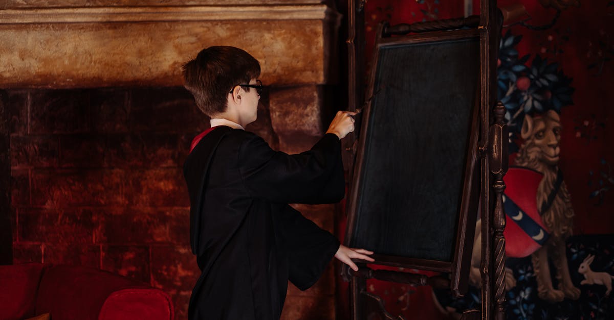 A young boy in a wizard costume writes on a blackboard in a fantasy-themed room.