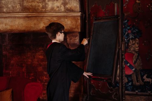 Free A young boy in a wizard costume writes on a blackboard in a fantasy-themed room. Stock Photo