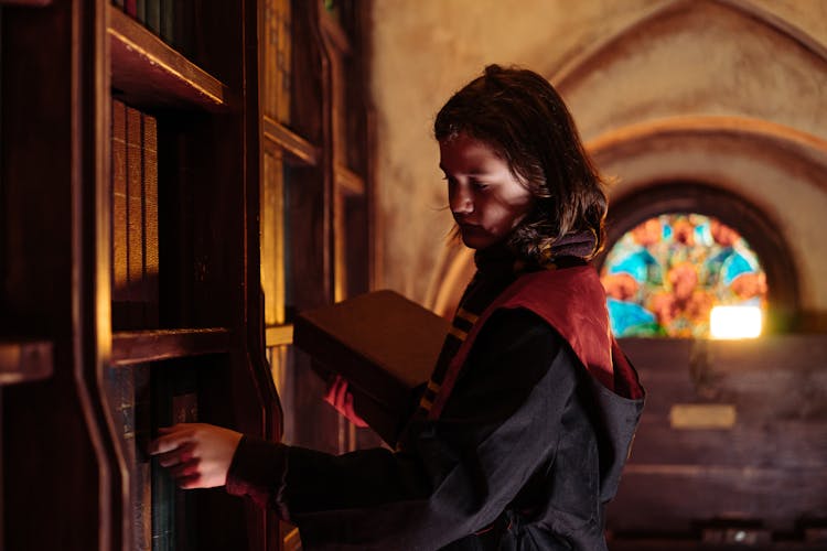 A Boy In A Harry Potter Costume Looking At A Bookshelf